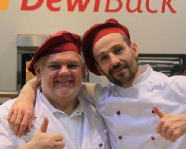 Zwei DewiBack Kollegen die sich freundschaftlich im Arm liegen und Daumen hoch zeigen
